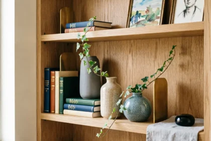 Style a bookshelf like a designer: A curated wooden display featuring stacked books, textured ceramic vases with trailing ivy, gold bookends, and framed art arranged with intentional negative space.